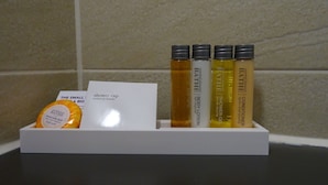 A hotel bathroom with a white shelf holding toiletries including a shower cap, body lotion, and conditioner. - Garner Hotel Preston Samlesbury (Preston)