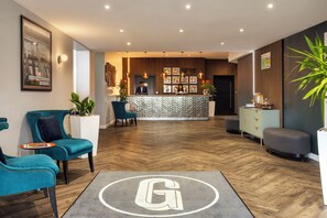 A hotel lobby with teal chairs, a reception desk, and a herringbone wood floor. - Garner Hotel Preston Samlesbury (Preston)