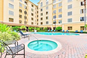 En hotellinnergård med en swimmingpool, solstolar och en möblerad sittplats under tak.