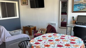 En stue med en sofa, et bord med et blomstret dug, et fjernsyn og en loftsvifte.