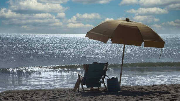 Une scène de plage avec une seule chaise de plage et un parasol.