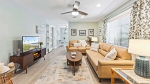 Un salon moderne avec un canapé, une table basse, un téléviseur et un ventilateur de plafond.