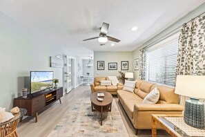 Ein modernes Wohnzimmer mit Sofa, Couchtisch, Fernseher und Deckenventilator.