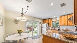 Une cuisine moderne avec des meubles en bois, un plan de travail en granit et un coin repas comprenant une table et des chaises.
