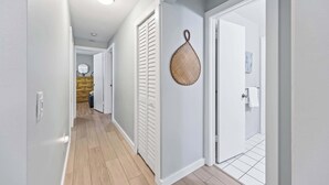 Un couloir aux murs blancs, avec un plancher en bois et une porte blanche sur laquelle est accrochée une serviette.