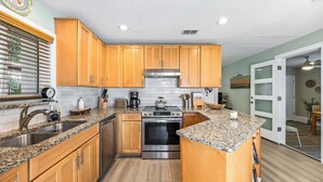 Une cuisine dotée de meubles en bois, de plans de travail en granit, d’appareils électroménagers en acier inoxydable et d’une fenêtre avec des stores.