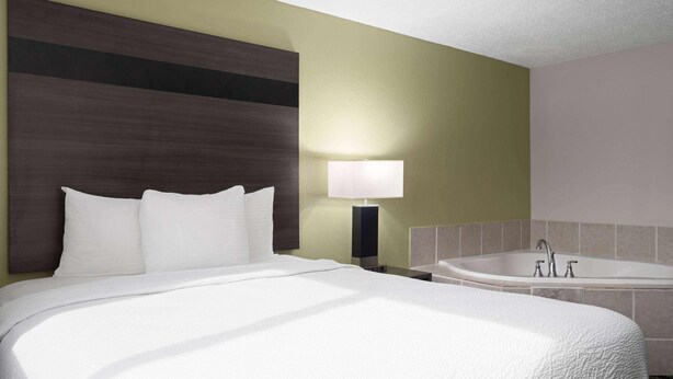 Ein Hotelzimmer mit Bett, Nachttisch, Lampe und Badewanne.