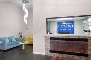 A hotel lobby with a reception desk, a fireplace, a blue sofa, and a yellow armchair. - Baymont by Wyndham Liberty MO (Liberty)