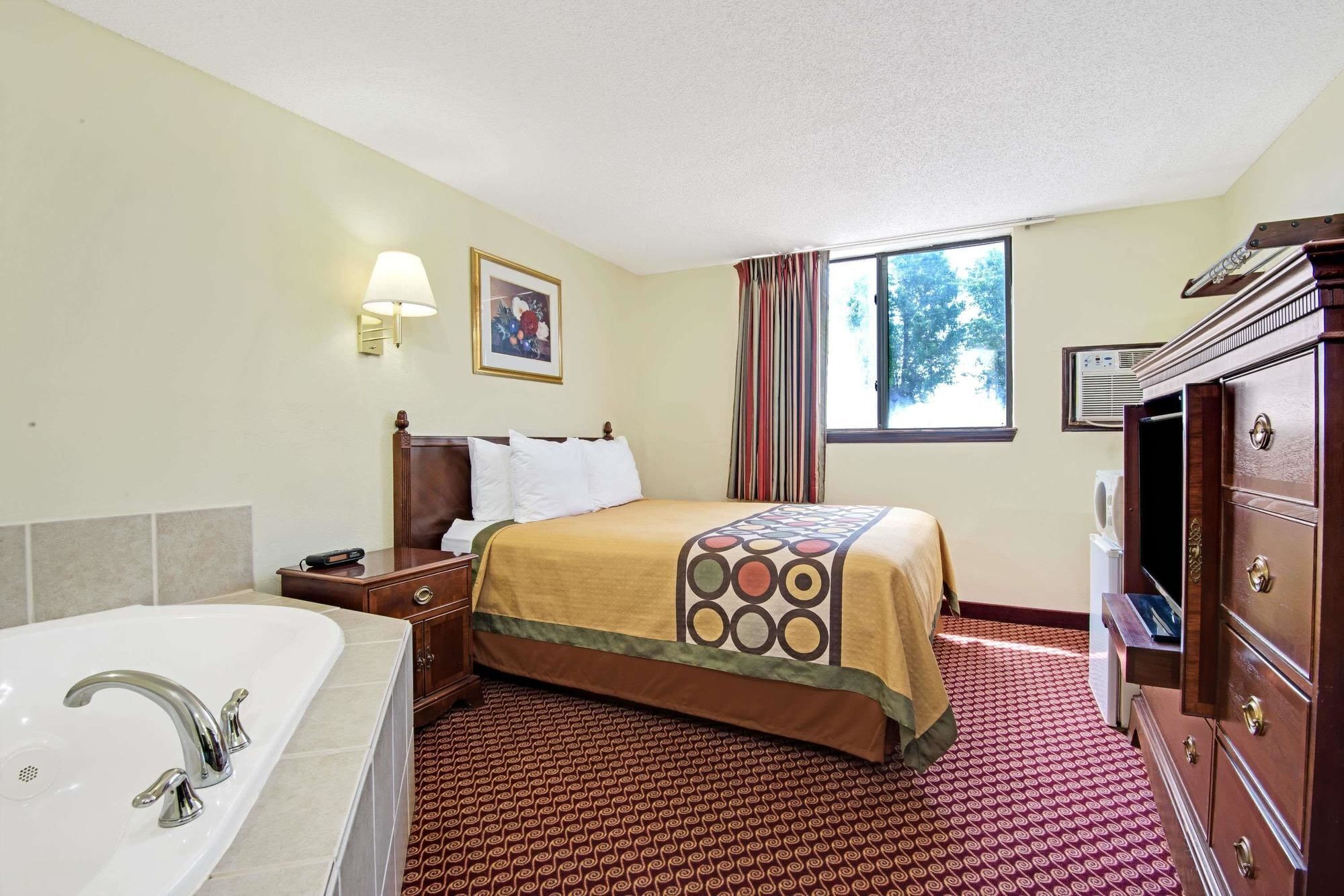 Een hotelkamer met een bed, een groot raam, een badkamer met een bad en een houten dressoir.