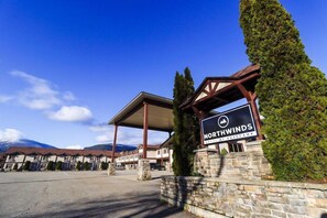 Entrada de un hotel con un letrero que dice 'Northwinds Hotel by Basecamp', una zona de estacionamiento techada y un paisaje montañoso de fondo.