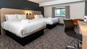 Une chambre d’hôtel avec deux lits, un bureau, une chaise et une fenêtre avec des rideaux.