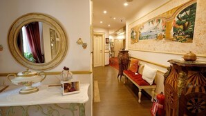 A hotel lobby with a round mirror, a white table with a decorative item, a sofa with red cushions, and a painting on the wall. - 2 Kitarrat Boutique Hotel and Spa (Durrës)