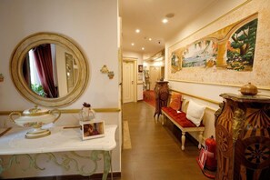 Un hall d’hôtel avec un grand miroir rond, une table blanche agrémentée d’un objet décoratif, un canapé avec des coussins rouges et un tableau accroché au mur.
