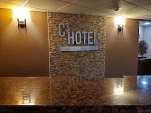 Un área de recepción con una pared de piedra, un letrero que dice 'C3 HOTEL HASTINGS, NEBRASKA' y dos luces empotradas.