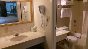 A hotel bathroom with a sink, toilet, and shower. There is a hairdryer mounted on the wall. - Motel6 Hastings, NE (Hastings)