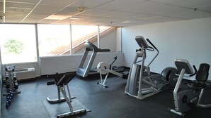Uma academia com esteiras, máquinas de musculação e pesos livres.
