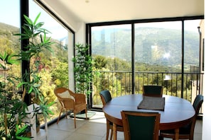Ein Balkon mit Esstisch und Stühlen, umgeben von Topfpflanzen, mit Blick auf eine Berglandschaft.