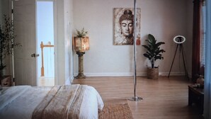 Ein Schlafzimmer mit einem Bett, einer Topfpflanze, einer Stehlampe, einem Gemälde und einem Stativ.