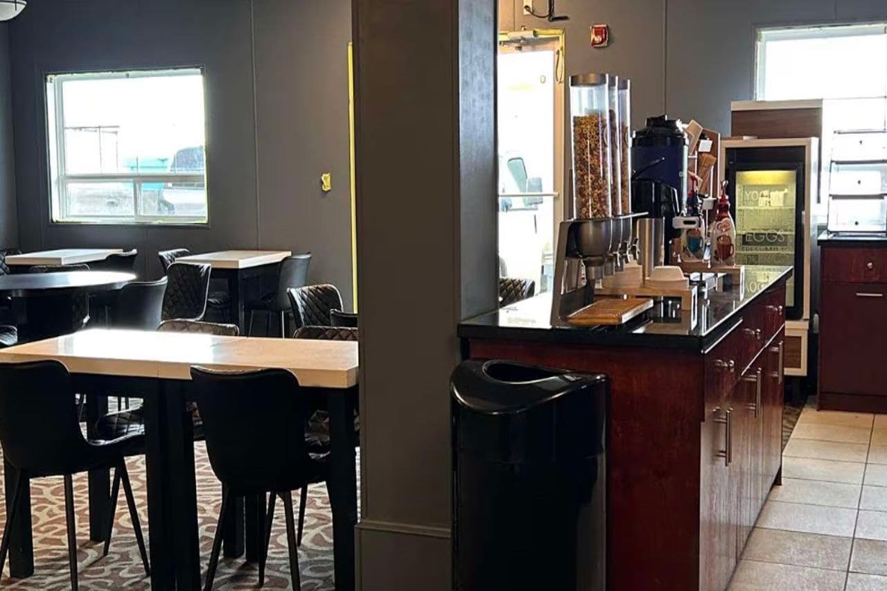 A restaurant with a counter, chairs, tables, and a trash bin.