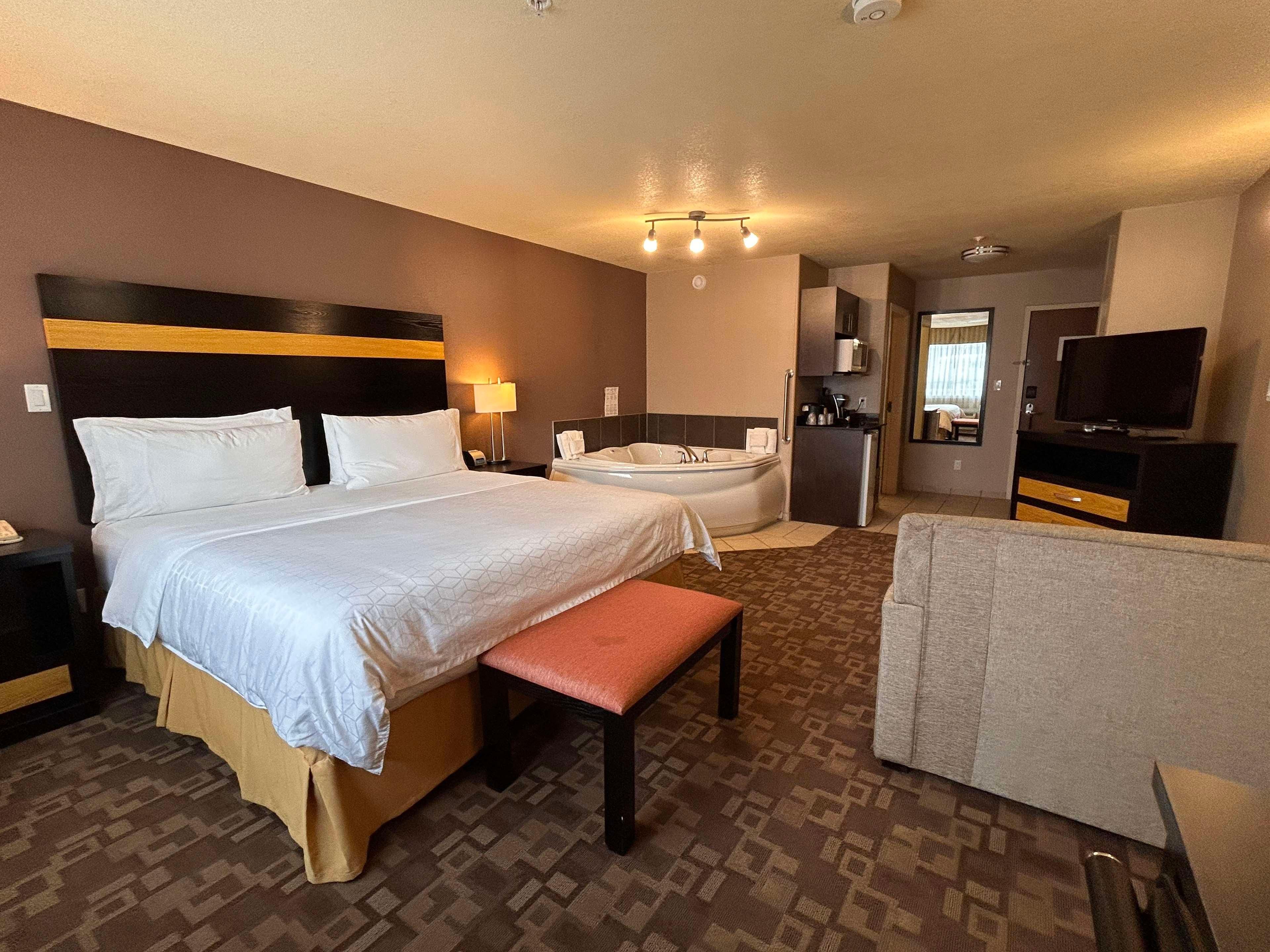 Une chambre d’hôtel avec un grand lit, un banc, une baignoire, une télévision et une kitchenette.