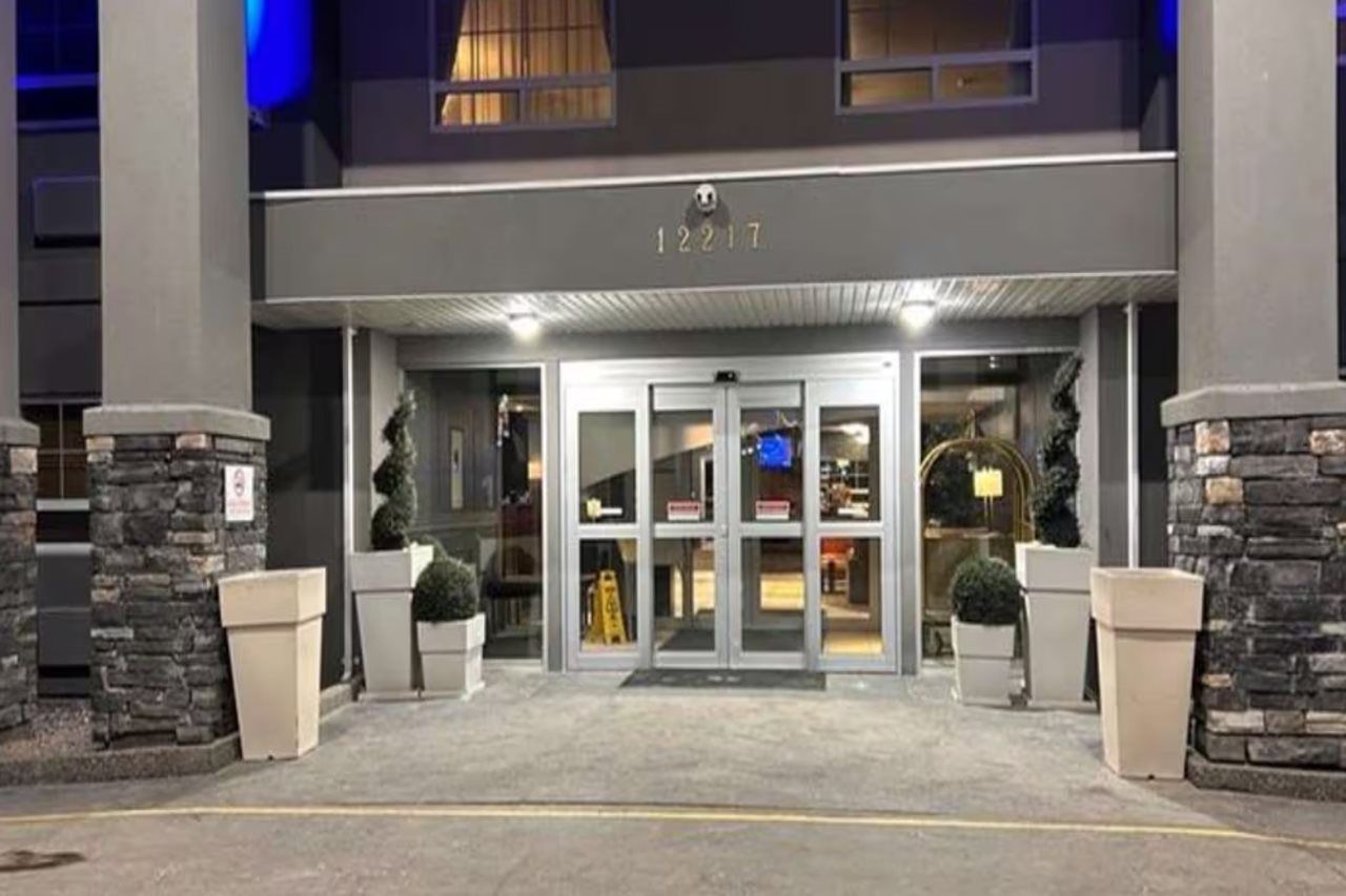 L’entrée d’un hôtel, avec une plaque portant le numéro de l’adresse, une porte vitrée et des plantes en pot.