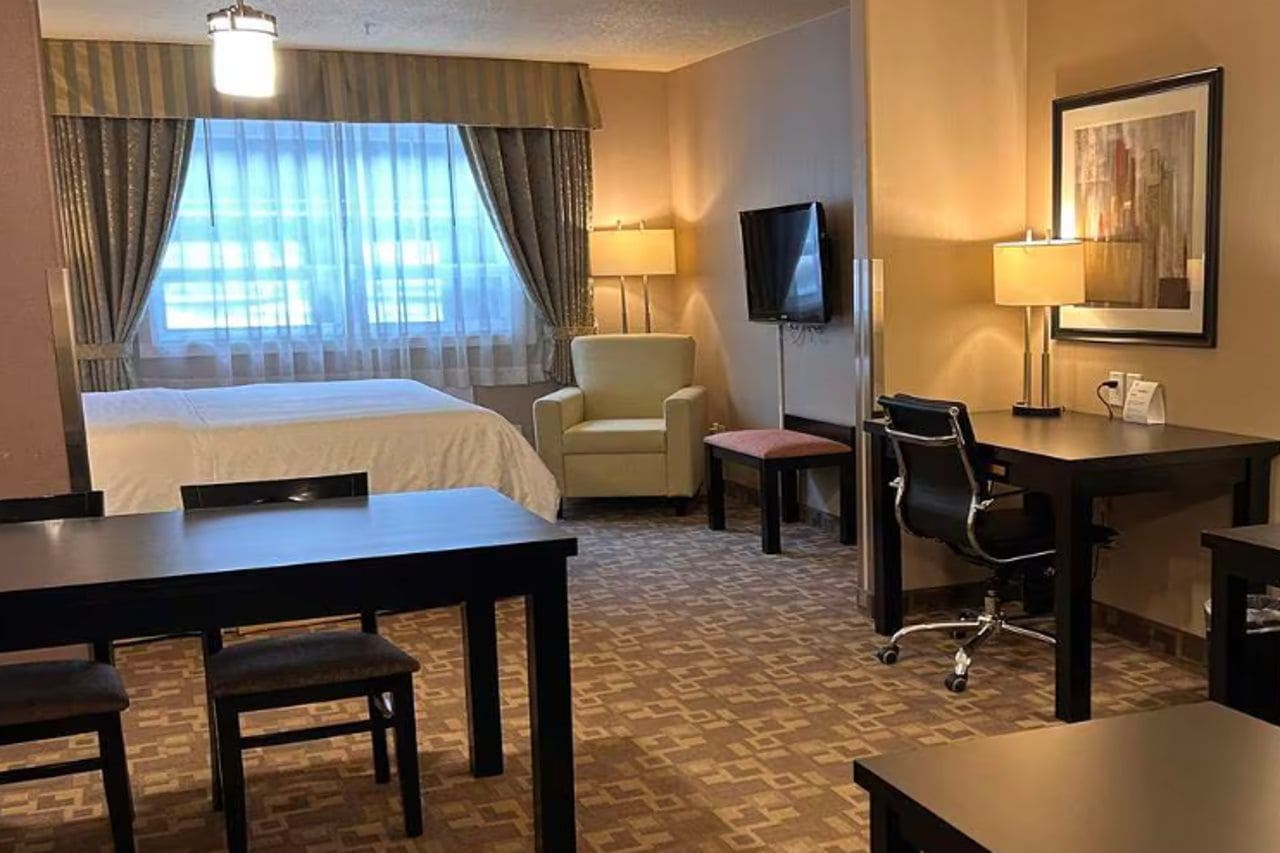 A hotel room with a bed, a desk, a chair, a television, and a lamp.