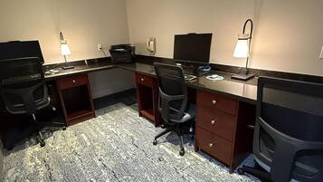 Habitación de hotel con escritorio, dos sillas, una impresora, teléfono y lámpara.