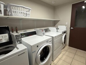 Una sala de lavandería con lavadora de carga frontal, lavasecadora apilada y secadora.