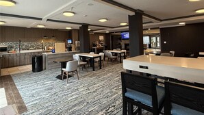 Un hall d'hôtel moderne avec un bar, des espaces pour s'asseoir et une cuisine en arrière-plan.