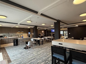 Un moderno vestíbulo de hotel con zona de bar, asientos y cocina al fondo.