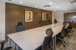 Un salón de conferencias con una larga mesa, varias sillas y dos cuadros en la pared.