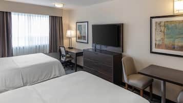 A hotel room with two beds, a desk, a chair, a television, and artwork on the wall.