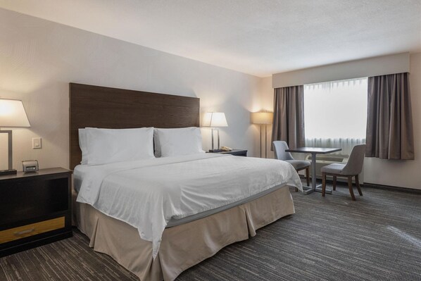 Una habitación de hotel con una cama grande, mesitas de noche, un escritorio con una silla y una ventana con cortinas.