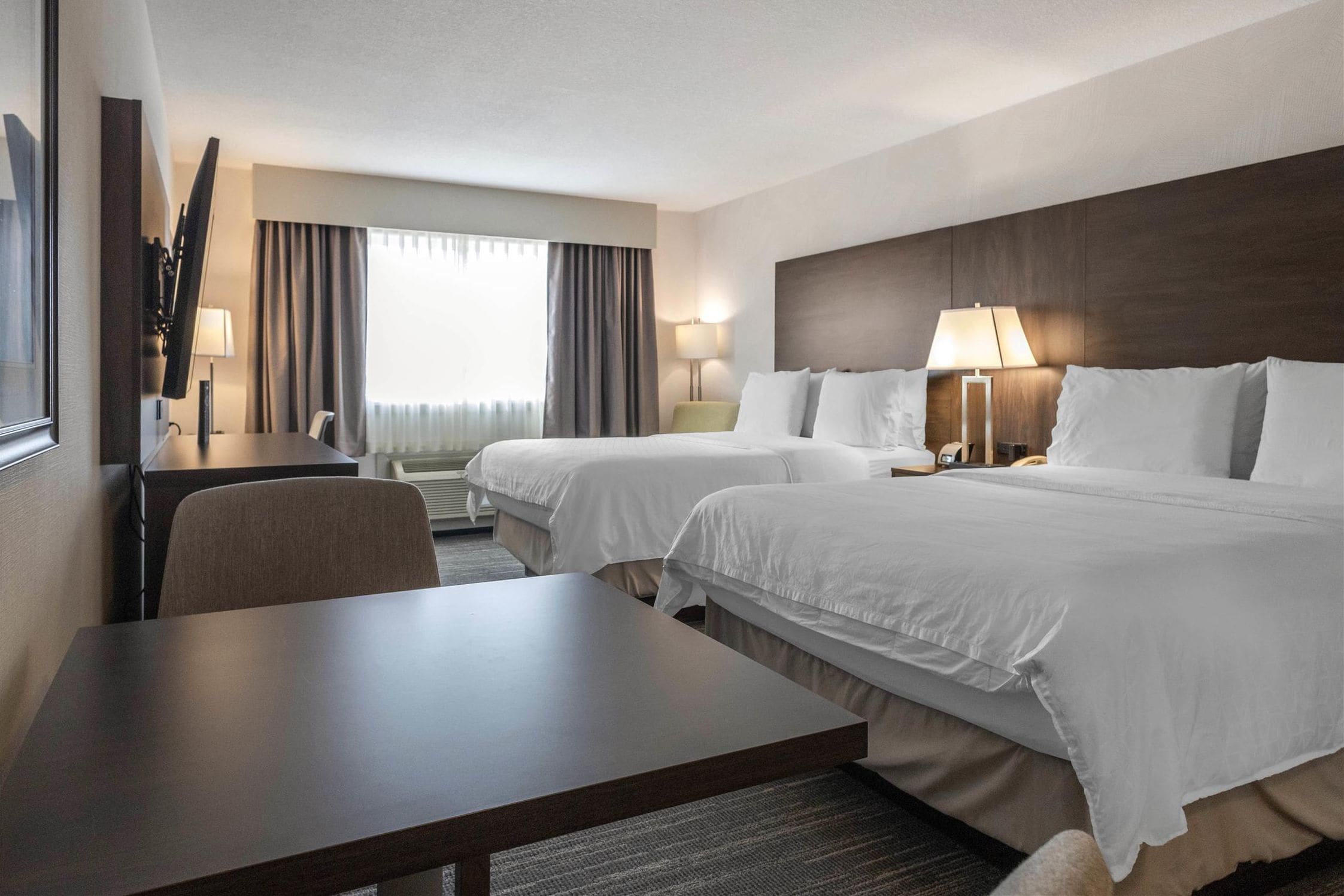 Une chambre d’hôtel avec deux lits, un bureau, une chaise, une télévision et une fenêtre avec des rideaux.