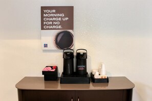 Una estación de café con un letrero, una cafetera, un termo y un portavasos.