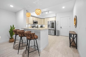 A modern kitchen with a central island, bar stools, stainless steel appliances, and pendant lighting. - RIVER FLY IN: The Meritt, River & Runway View (Merritt Island)
