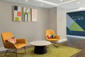 Quarto moderno com duas cadeiras laranja, uma mesa redonda e arte abstrata na parede.