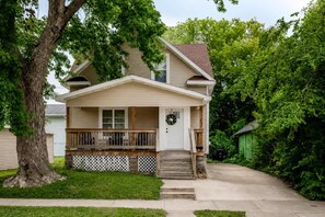 A two-story house with a front porch, a visible front door, and a small front yard.