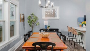 Un espace repas comprenant une table en bois, des chaises noires, une décoration centrale en fibres tressées et un luminaire suspendu.