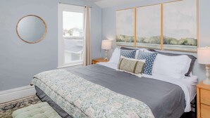 Une chambre à coucher avec un lit, des tables de chevet, une fenêtre et une vue sur l’extérieur.