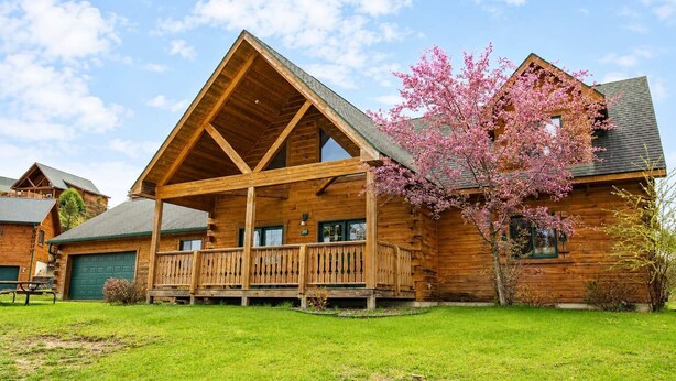 Eine Blockhütte mit Veranda, Garage und blühendem Kirschbaum.