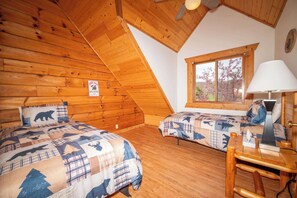 A cabin with two beds, a wooden ceiling, a window with a view, and a lamp on a table.