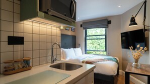 Habitació d'hotel moderna amb un llit gran, un lavabo integrat, una televisió de pantalla plana i una finestra amb vistes a la vegetació.