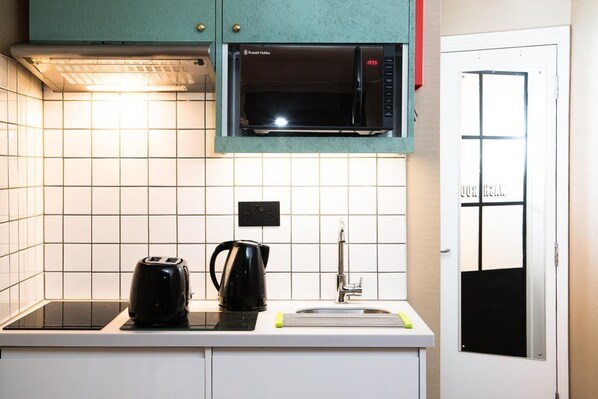 A kitchen with a microwave, a kettle, and a sink.