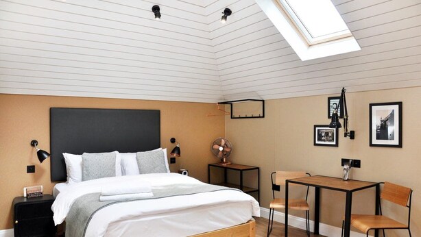 A bedroom with a bed, bedside tables, a desk, chairs, a fan, and a skylight. - Room2 Hammersmith Hometel (London)