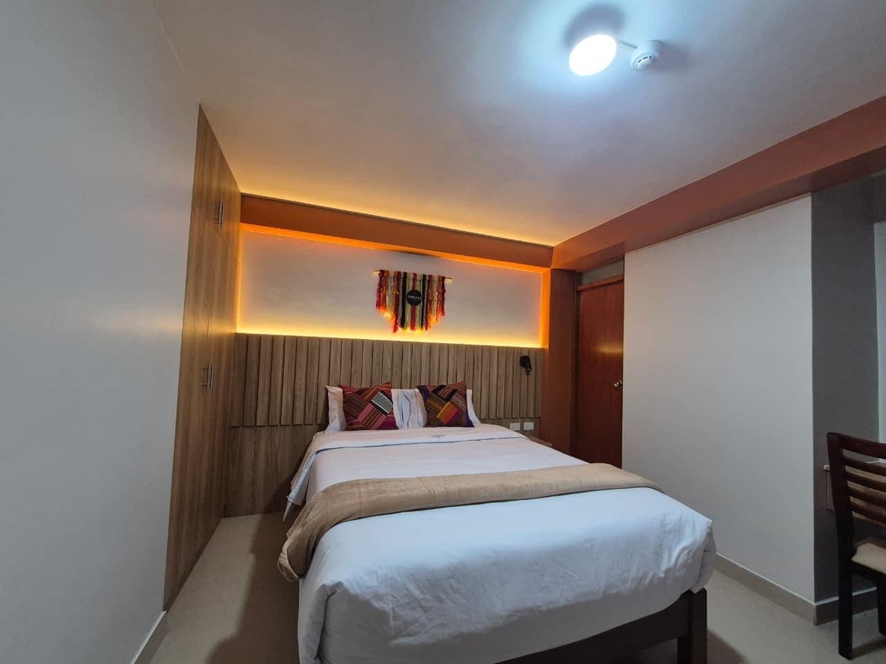 A hotel room with a bed, a desk, and a wall-mounted light fixture.