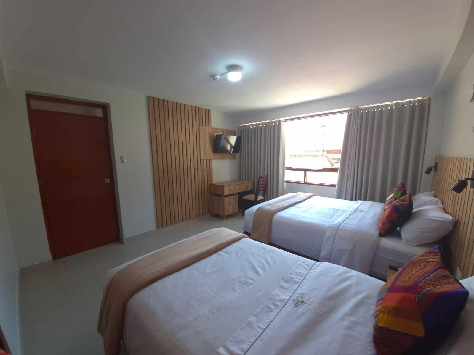 A hotel room with two beds, a desk, a chair, a TV, and a window with curtains.