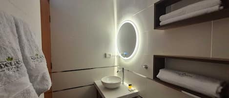 A modern bathroom with a round mirror, a sink, and a toilet. There are towels on a shelf and a towel hanging on the wall.