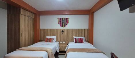 A room with two beds, wooden headboard, a wall-mounted TV, and a ceiling fan.
