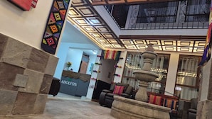 A lobby with a stone fountain, a reception desk, and a seating area with a chair and a sofa. - Adolfos Hotel Cusco (Cusco)